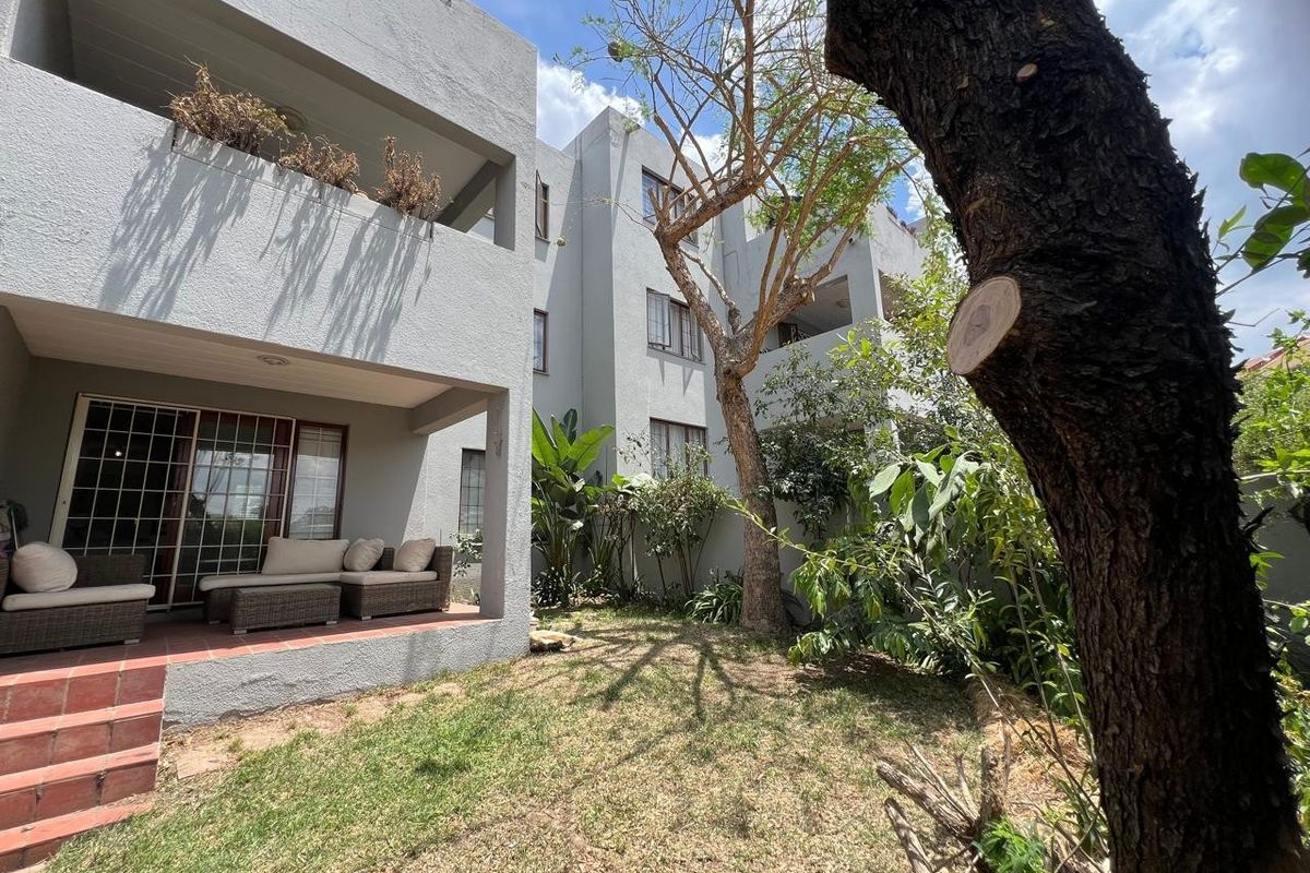 A ground-floor apartment exterior featuring a covered patio area, tiled steps, and a private garden space with mature trees.