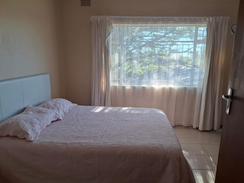 A bedroom featuring tiled flooring and a large window with security bars, allowing natural light into the space.