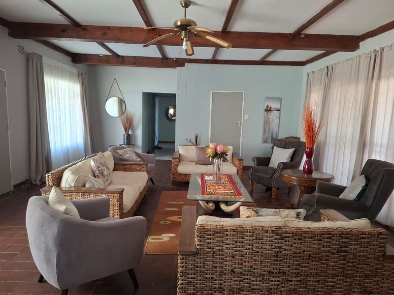 Spacious living room featuring exposed timber ceiling beams, terracotta floor tiles, and large windows allowing for ample natural light.