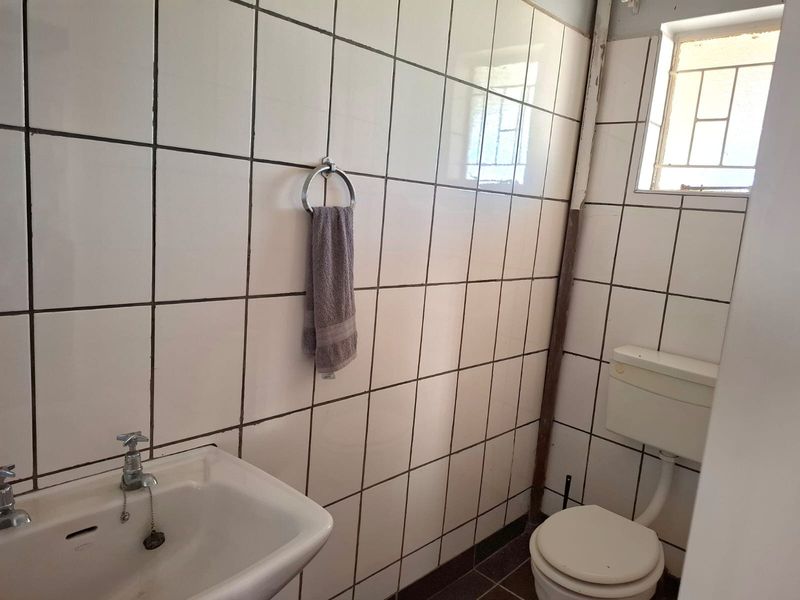 A compact bathroom featuring white wall tiles, a standard pedestal basin, and a toilet with a high-level cistern.