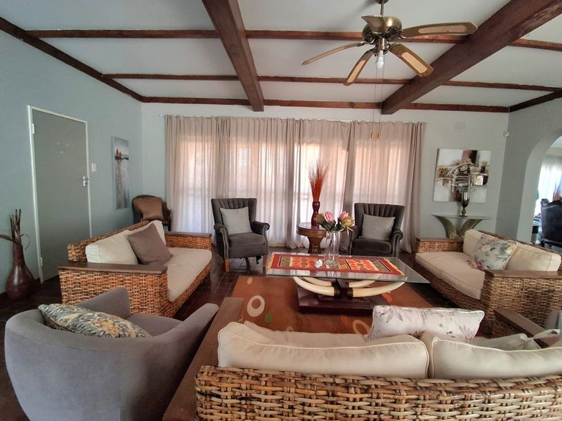 Spacious living room featuring exposed timber ceiling beams, a ceiling fan, and large windows with floor-to-ceiling curtains.