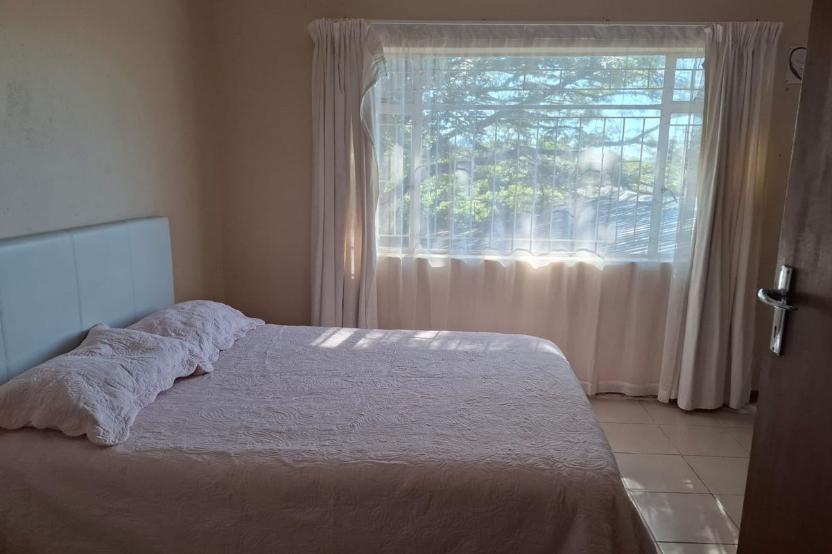 A bedroom featuring tiled flooring and a large window with security bars, allowing natural light into the space.