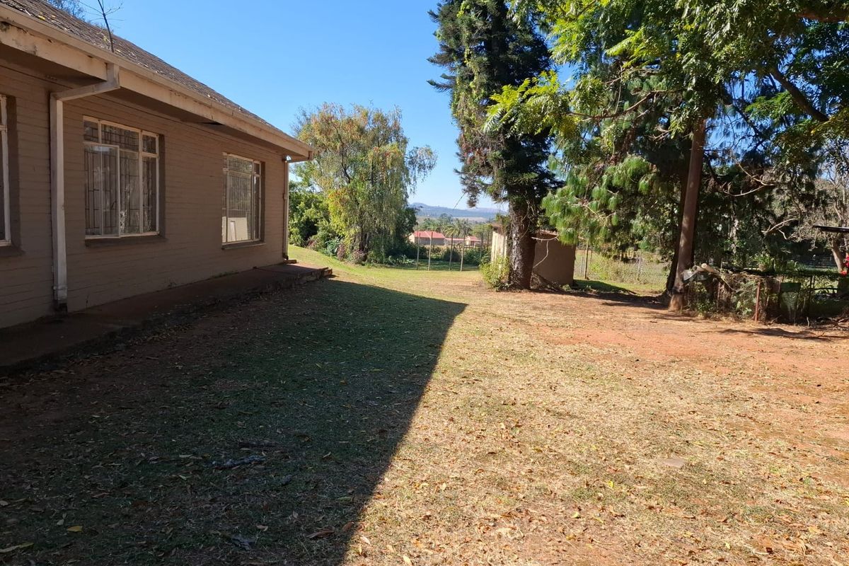 A view of the rear exterior of the property, featuring a large garden area with mature trees and a view of the surrounding landscape.