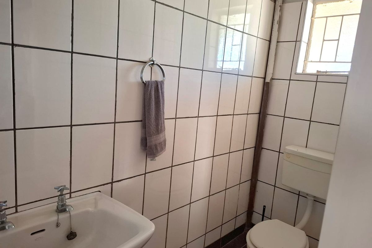 A compact bathroom featuring white wall tiles, a standard pedestal basin, and a toilet with a high-level cistern.