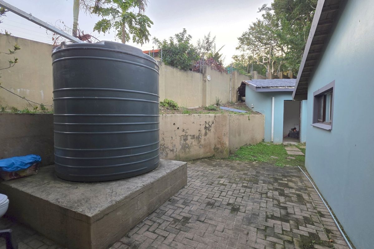 Rear exterior area featuring a large water storage tank on a concrete plinth, paved ground, and perimeter boundary walls.
