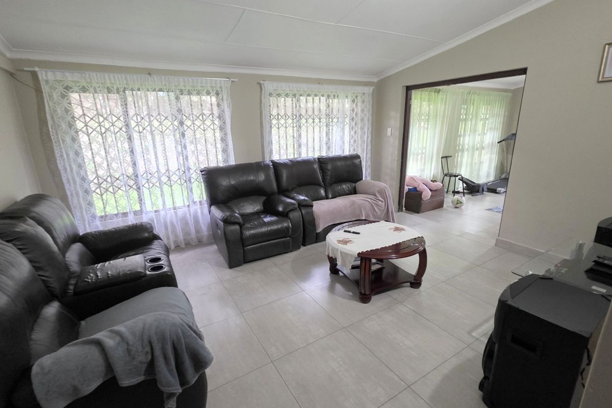 A spacious living room featuring large windows with security gates, neutral tiled flooring, and a seamless transition into an adjacent room.