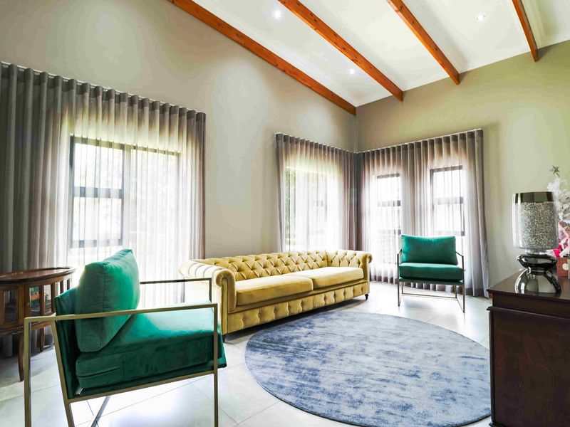 Spacious living room featuring high vaulted ceilings with exposed timber beams, large windows with floor-to-ceiling curtains, and neutral tiled flooring.