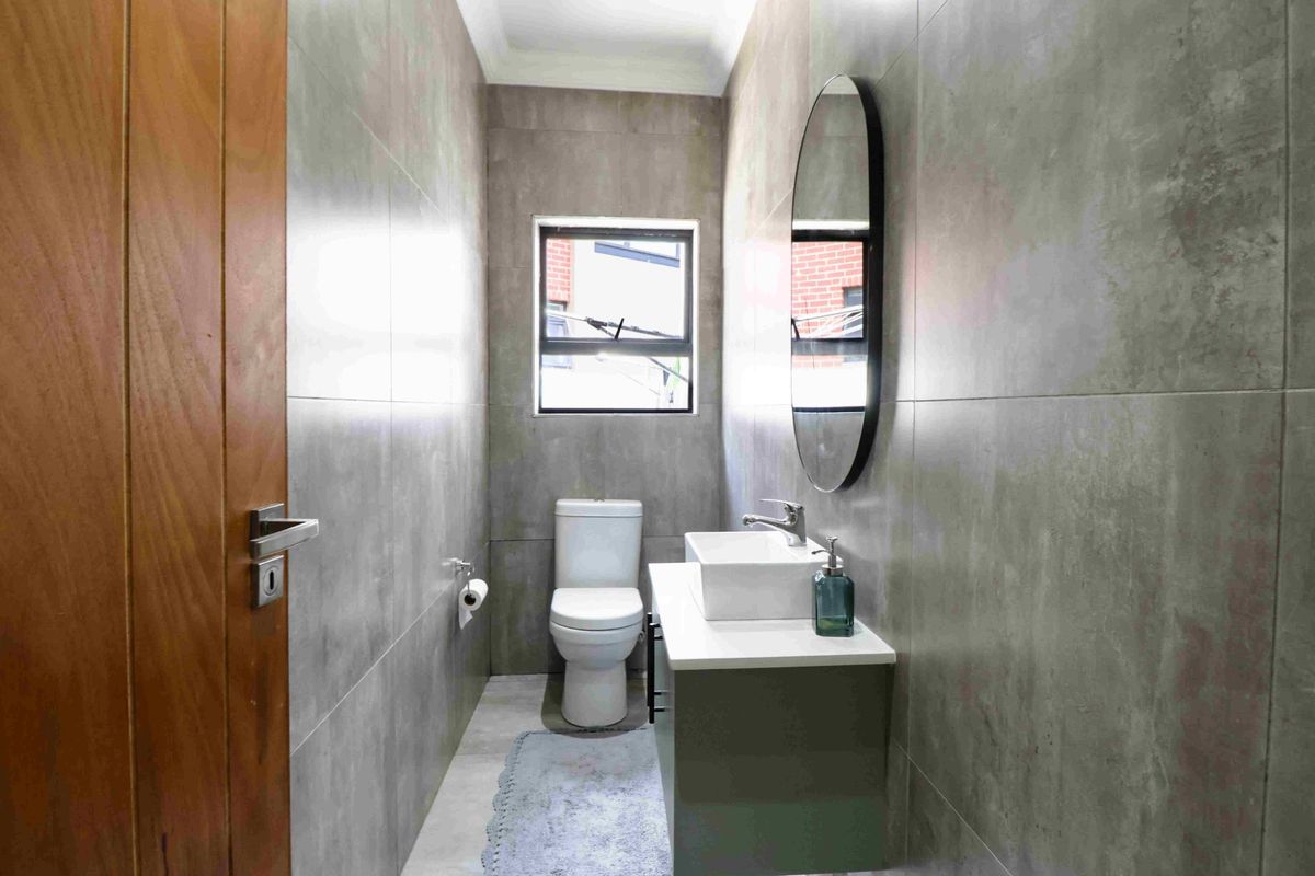 A modern, compact bathroom featuring floor-to-ceiling grey tiling, a sleek vanity with a vessel sink, and a contemporary toilet.