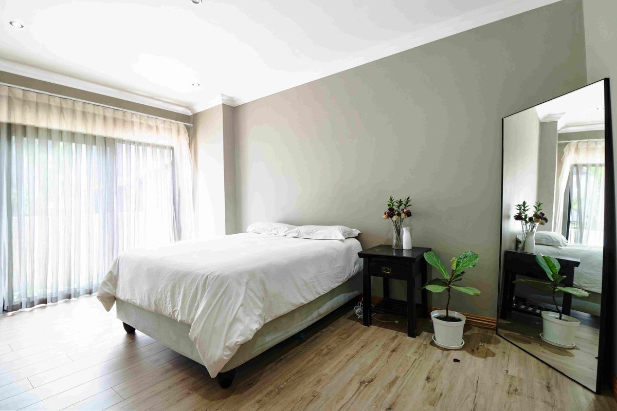 A well-lit bedroom featuring wood-look flooring, neutral wall tones, and large sliding glass doors with sheer curtains providing natural light.