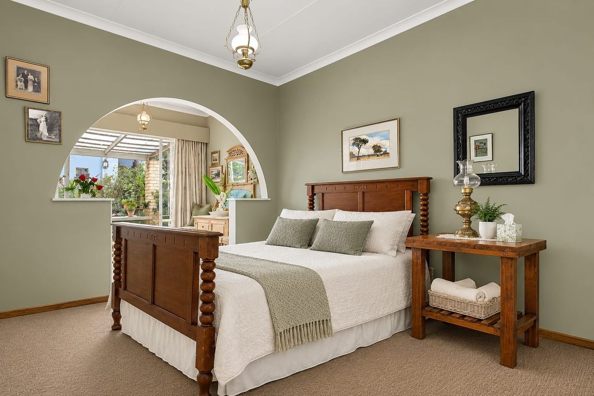 A well-maintained bedroom featuring a decorative arched opening leading to an adjoining sunroom, neutral wall tones, and carpeted flooring.