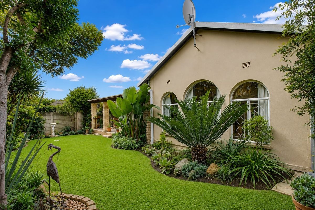 A well-maintained rear garden featuring a lush lawn, established landscaping, and a covered patio area adjacent to the house.