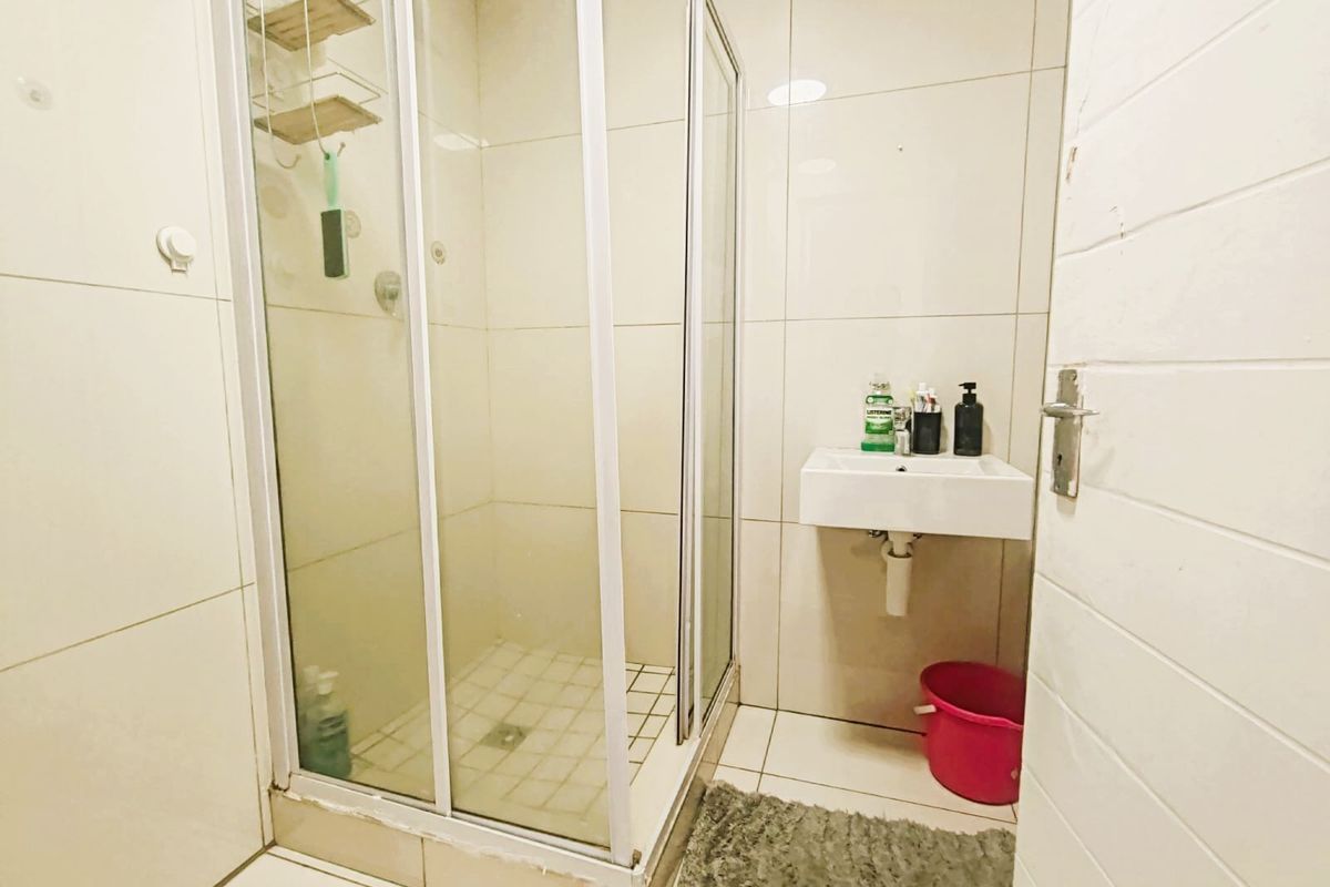 Compact bathroom featuring a glass-enclosed shower and a wall-mounted basin with neutral ceramic tiling throughout.
