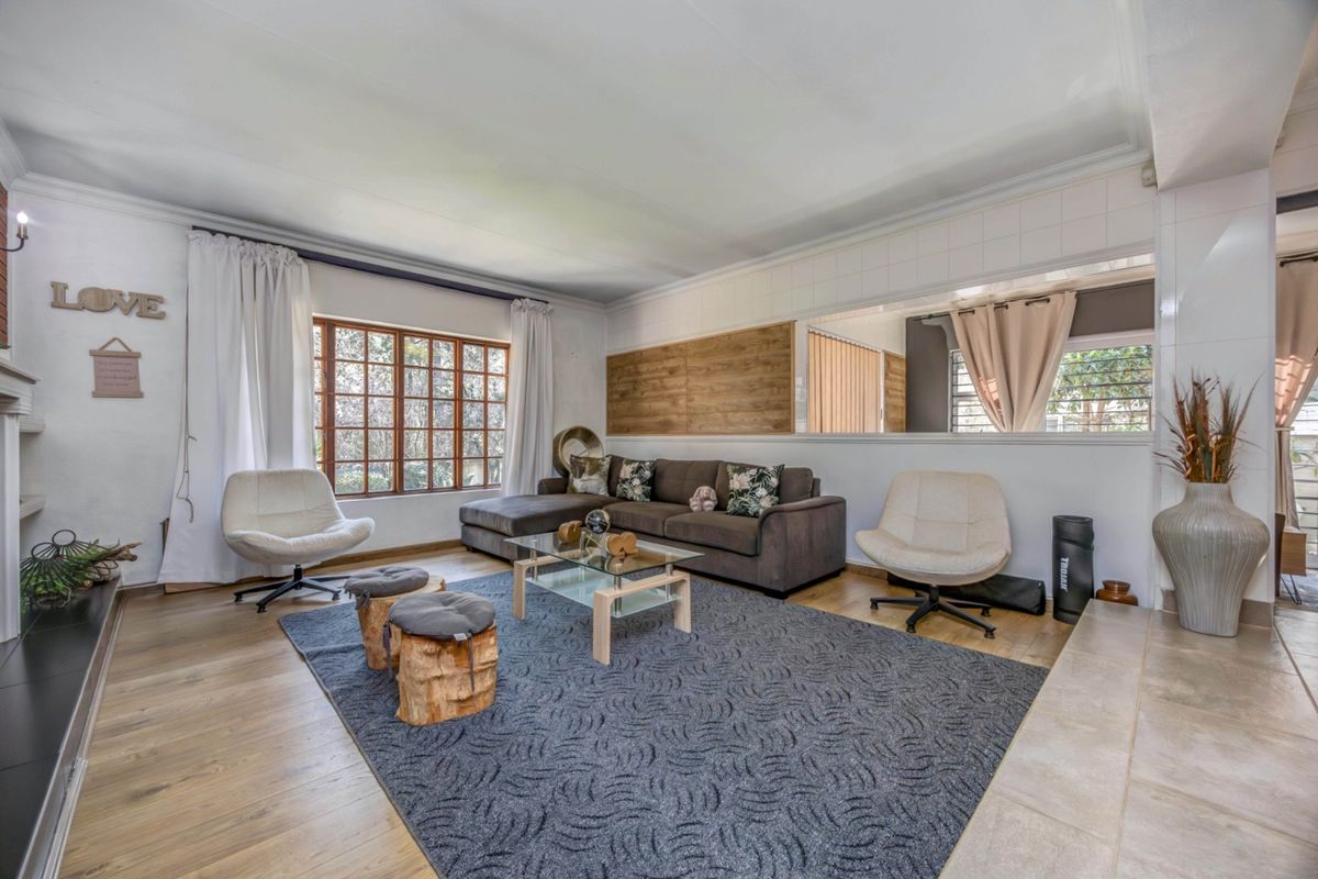 A spacious living room featuring timber-look flooring, a large window, and a partial wall partition with a serving window opening to an adjacent space.