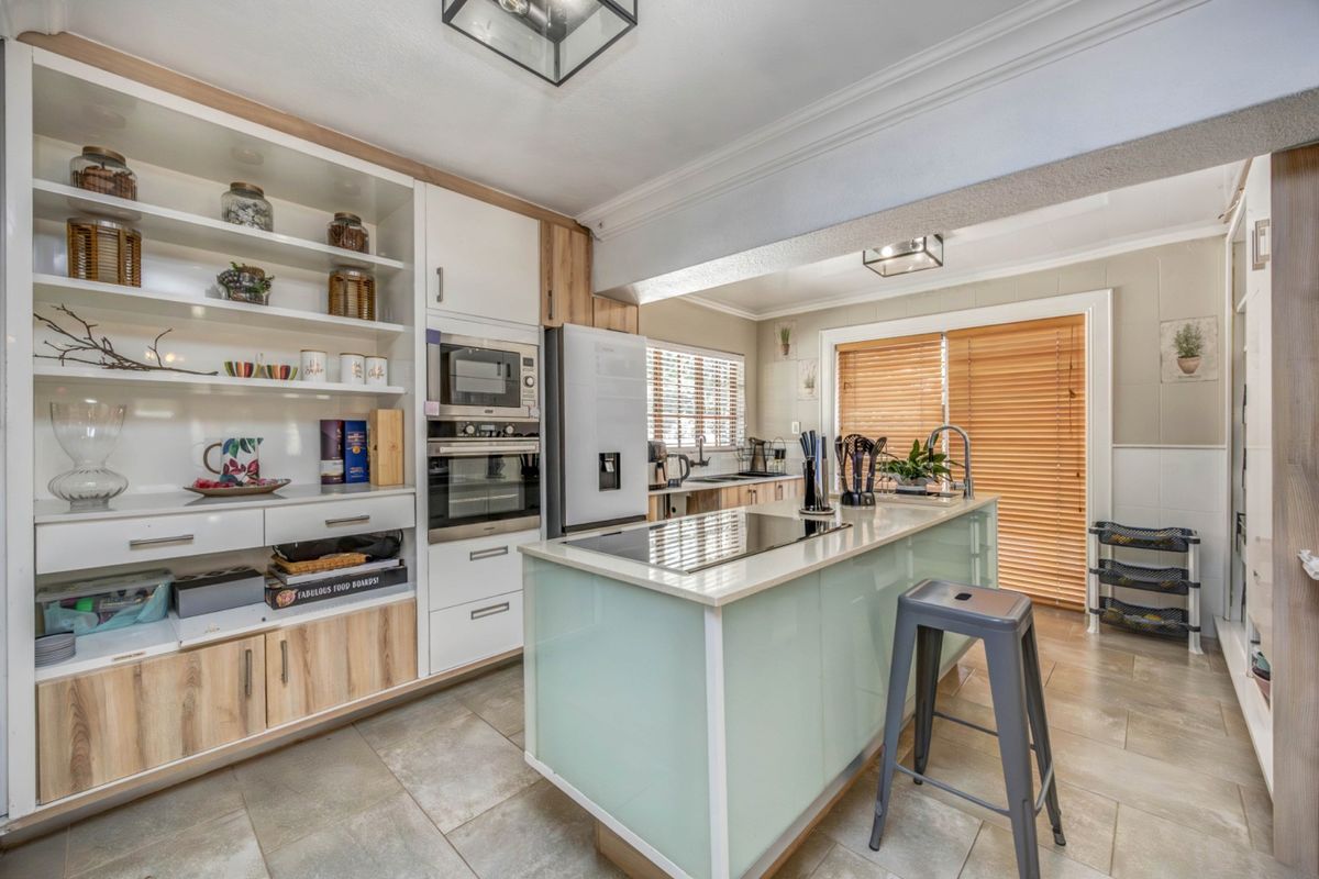 Modern kitchen featuring a central island with integrated cooktop, built-in oven and microwave, ample cabinetry, and tiled flooring with access to the patio.