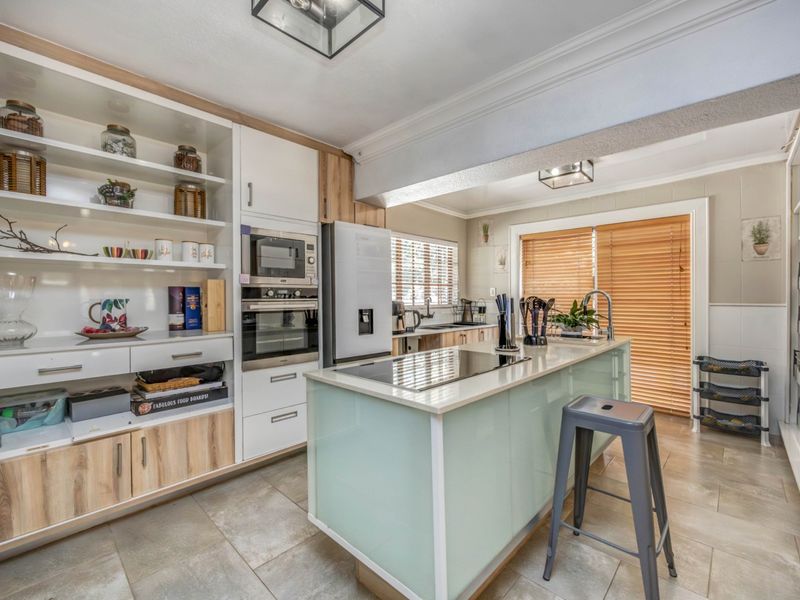 Modern kitchen featuring a central island with integrated cooktop, built-in oven and microwave, ample cabinetry, and tiled flooring with access to the patio.