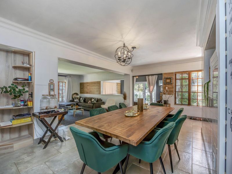 Spacious open-plan dining area featuring tiled flooring, crown molding, and large windows, seamlessly flowing into the adjacent living room.
