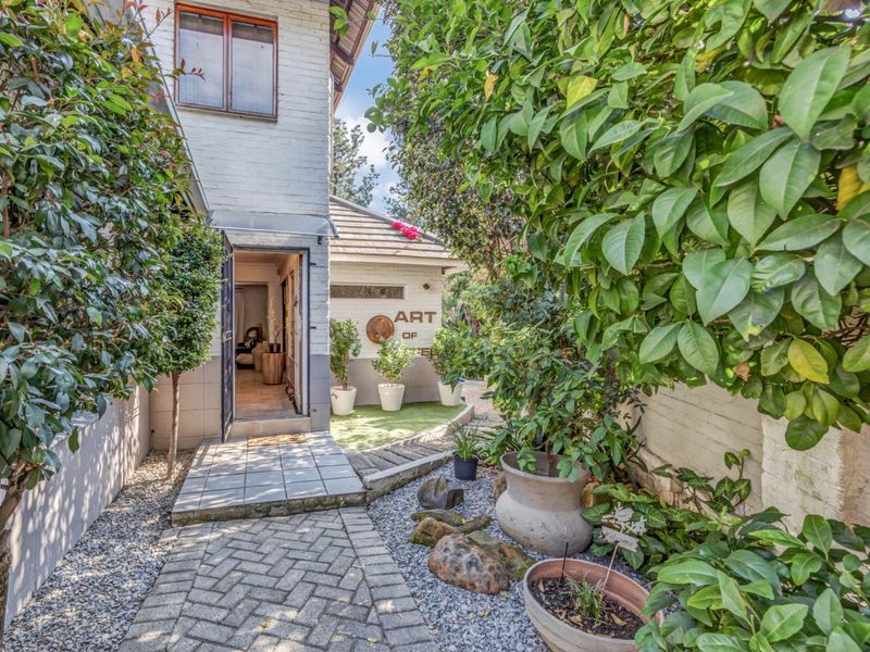 A charming side entrance pathway featuring paved walkways, landscaped garden beds, and a welcoming exterior door leading into the home.