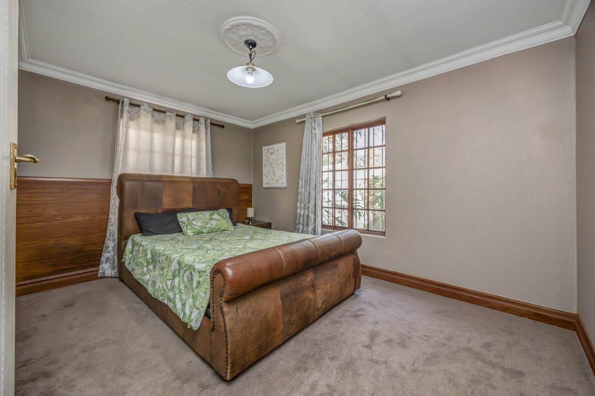 A bedroom featuring wood wall paneling, crown molding, a ceiling rose, and a window with security bars.