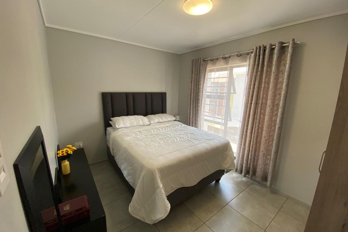 A well-maintained bedroom featuring neutral wall tones, tiled flooring, and a sliding door providing access to the exterior.