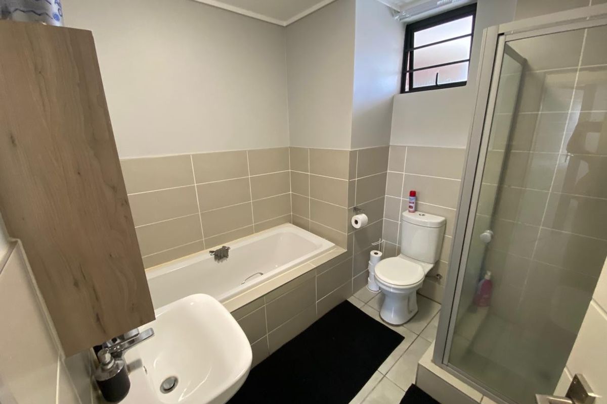 A functional bathroom featuring a built-in bathtub, separate glass-enclosed shower, pedestal basin, and toilet with neutral wall tiling.