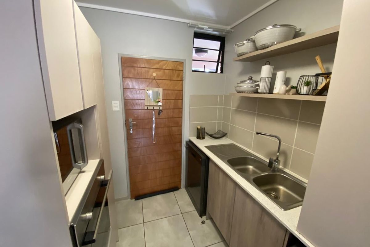 A compact, functional kitchen featuring built-in cabinetry, a double stainless steel sink, tiled backsplash, and integrated oven and microwave units.
