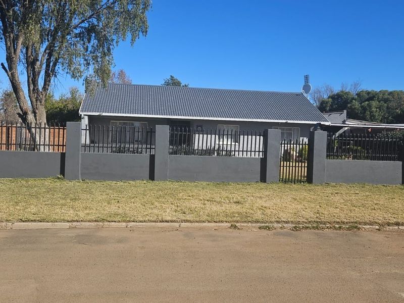 Front view of a single-story house featuring a dark grey tiled roof and a secure perimeter wall with integrated metal fencing.
