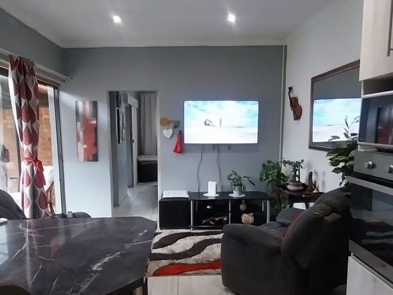 An open-plan living area featuring a modern kitchen with built-in oven and microwave, flowing into a comfortable lounge space with direct patio access.