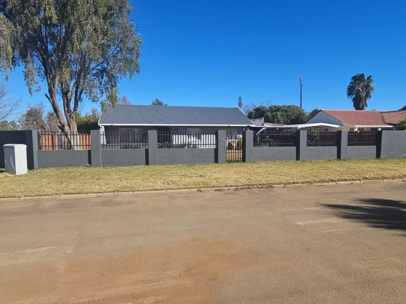 A street-level view of the property featuring a modern dark grey perimeter wall with integrated metal fencing and a well-maintained front lawn.