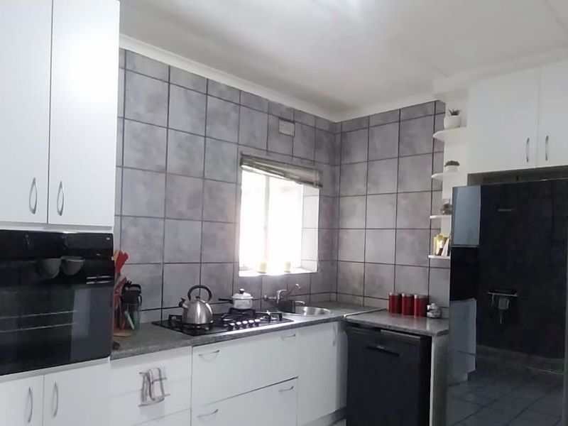 A functional kitchen featuring white cabinetry, built-in oven, gas hob, and grey tiled walls with ample counter space.