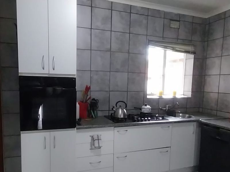 A functional kitchen featuring white cabinetry, built-in oven, gas hob, and grey tiled walls with a window providing natural light.