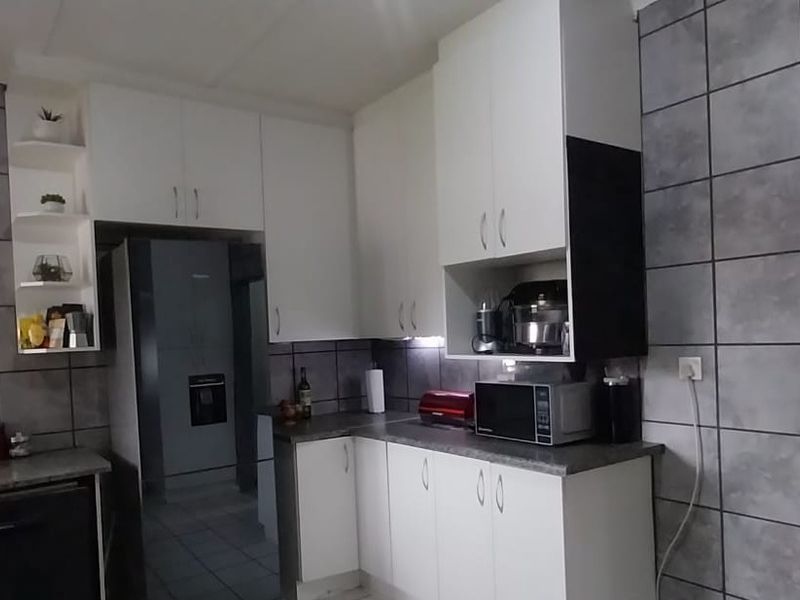 A functional kitchen featuring white cabinetry, grey tiled walls, and a dedicated scullery area for additional storage and preparation space.