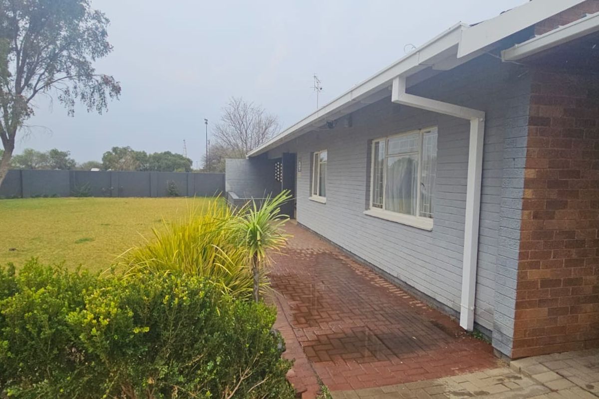 Rear view of the property featuring a brick facade, paved walkway, and a spacious garden area enclosed by a boundary wall.