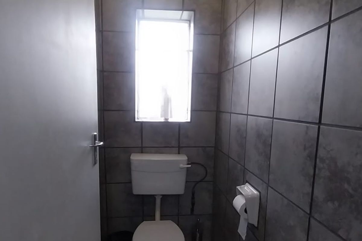 A compact bathroom featuring dark grey wall tiles, a standard white toilet, and a small window for natural light.