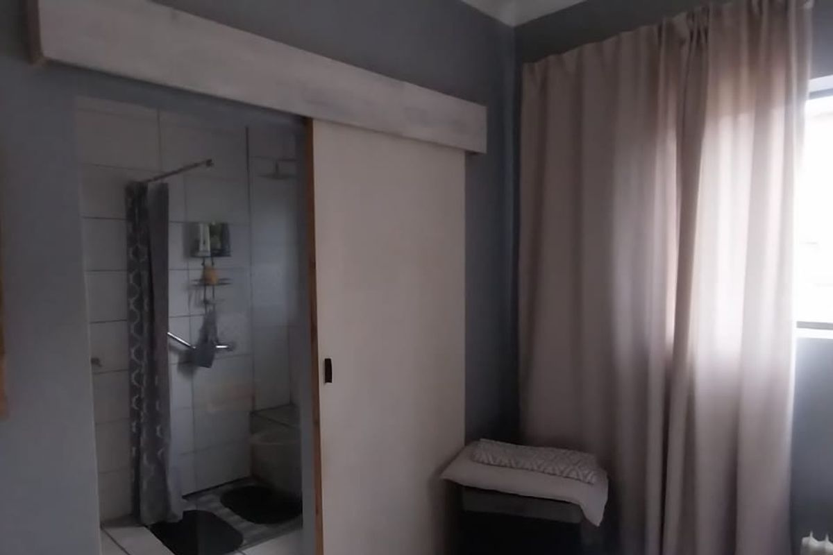 A bedroom featuring a sliding door entry to an en-suite bathroom, large window with curtains, and neutral wall finishes.
