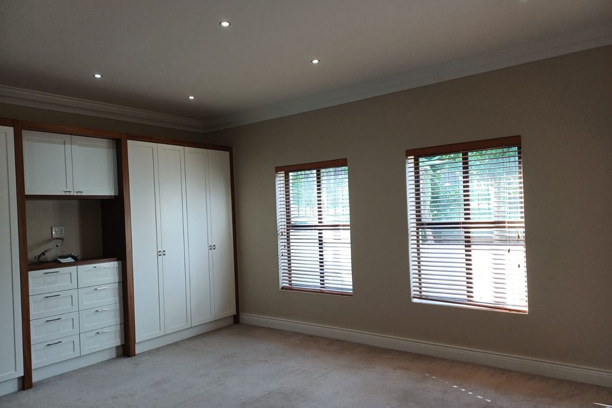 A spacious bedroom featuring neutral carpeting, recessed downlighting, and extensive built-in cabinetry with integrated storage and shelving.