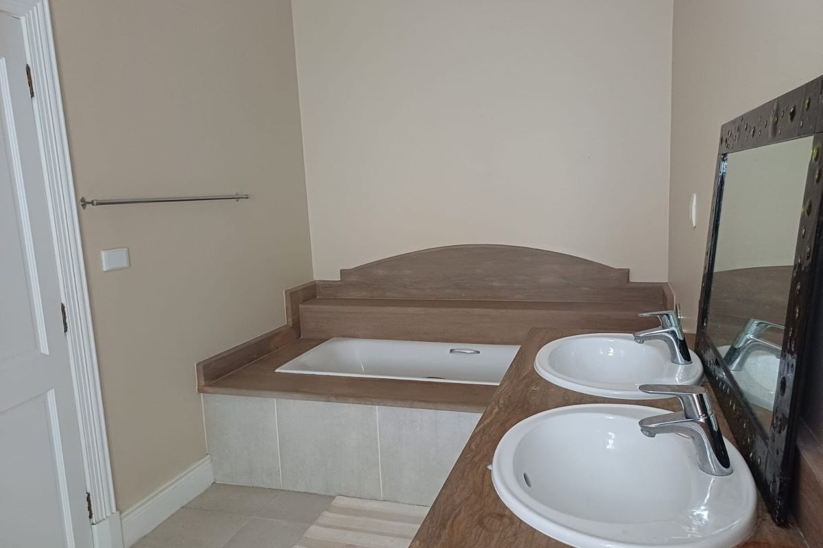 A functional bathroom featuring a built-in bathtub with tiled surround and a double vanity with drop-in sinks and chrome fixtures.