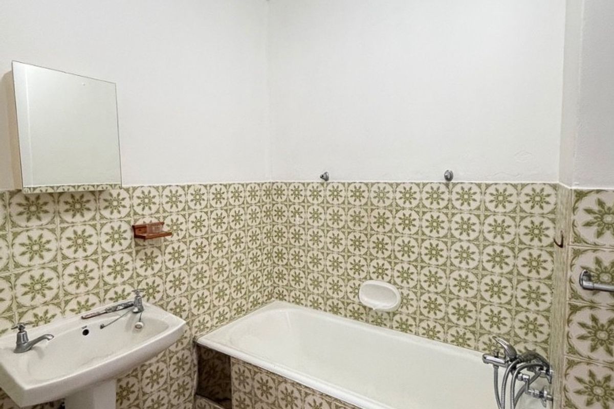 A dated bathroom featuring a pedestal sink, a built-in bathtub with shower mixer, and vintage patterned wall tiles.