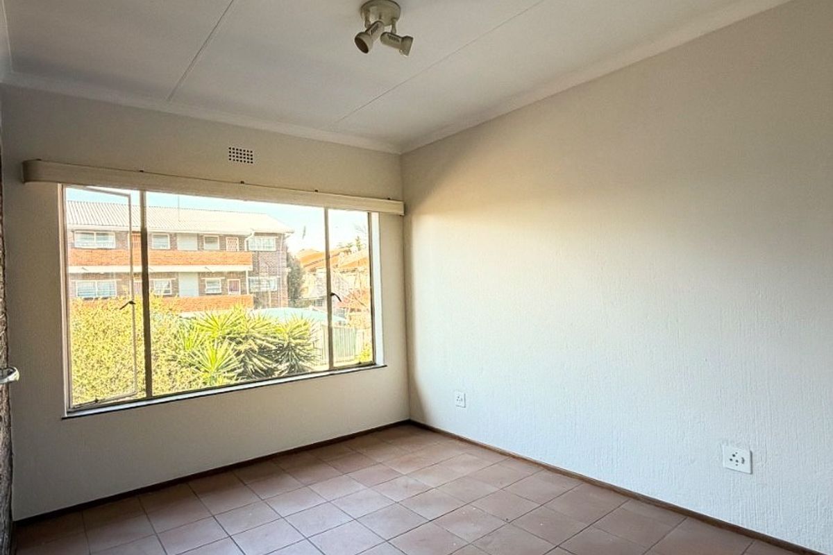 A bright, empty bedroom featuring tiled flooring, a large window with natural light, and a ceiling-mounted light fixture.
