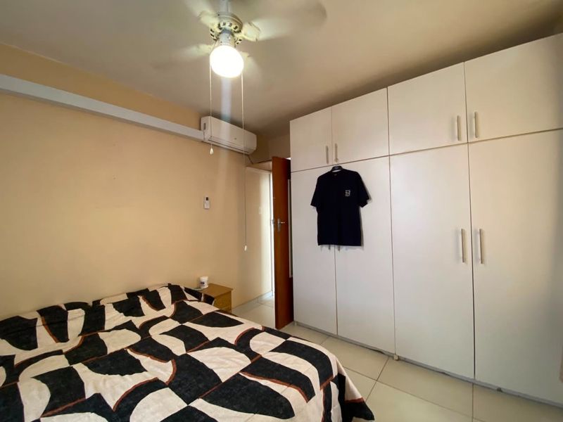 A bedroom featuring built-in floor-to-ceiling wardrobes, a ceiling fan, and a wall-mounted air conditioning unit.