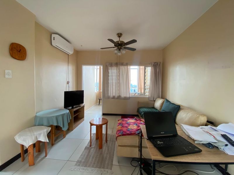 A functional living room featuring tiled flooring, a ceiling fan, and a wall-mounted air conditioning unit, with direct access to an adjoining balcony.