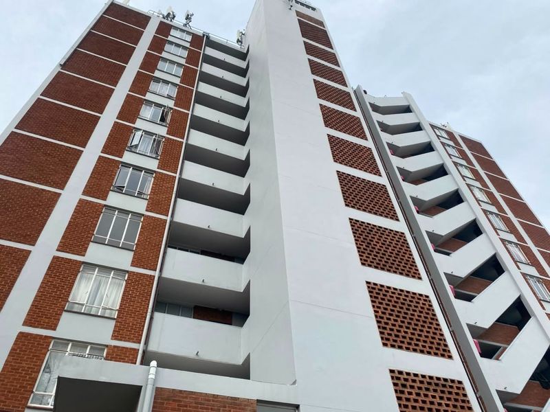 Low-angle view of a multi-story apartment building featuring a combination of red brick and painted concrete facade with integrated balcony structures.