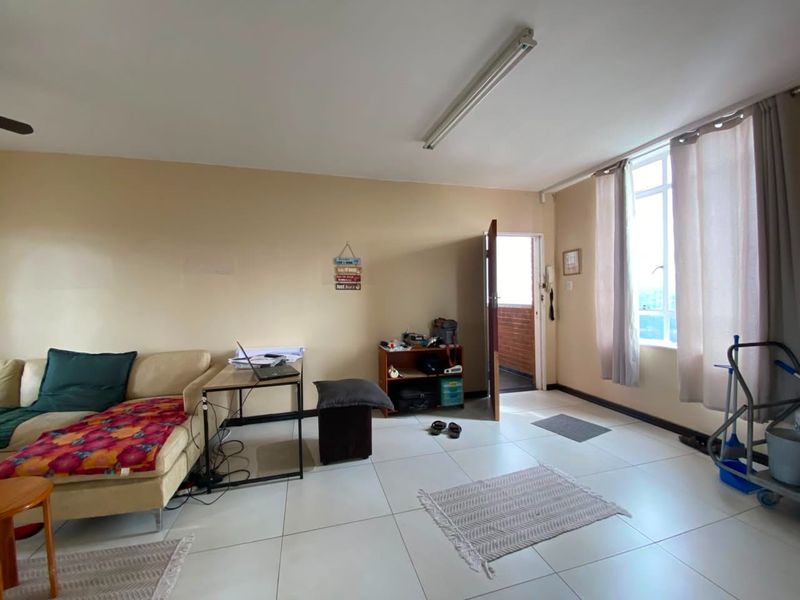 A spacious living area featuring large format floor tiles, natural light from a window, and direct access to an external walkway.