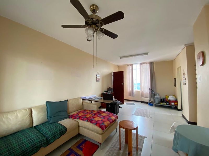 A spacious living area featuring tiled flooring, a ceiling fan, and large windows allowing for natural light.