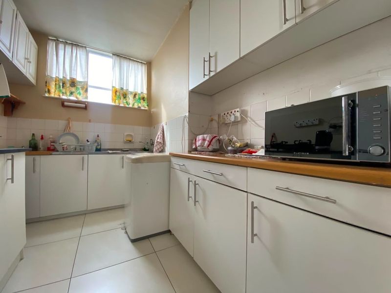 A functional kitchen featuring white cabinetry, wood-look countertops, tiled splashbacks, and tiled flooring with a dedicated space for a washing machine.