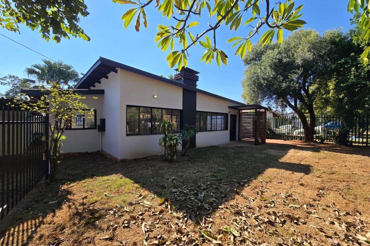 A view of the rear exterior of the house featuring a chimney, metal window frames, and a private garden area with perimeter fencing.
