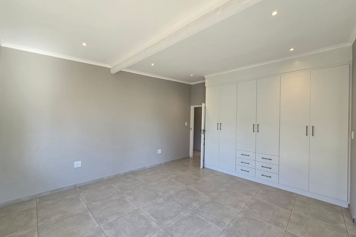 A spacious bedroom featuring neutral tiled flooring, recessed ceiling lighting, and extensive built-in cabinetry with ample storage space.