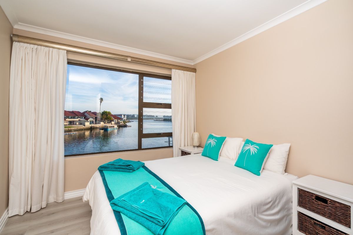 A bright bedroom featuring large windows with scenic water views, neutral wall tones, and modern light-colored flooring.