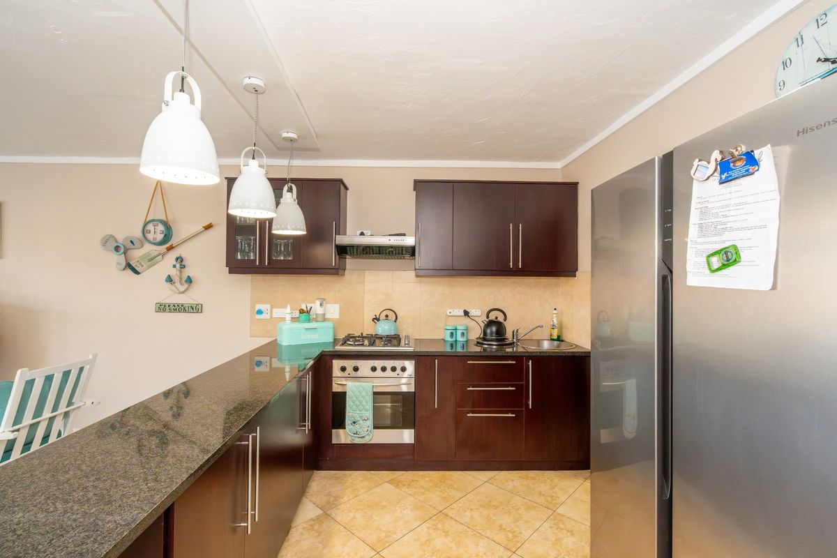 A compact kitchen featuring dark wood cabinetry, granite countertops, a built-in oven with gas hob, and tiled flooring.