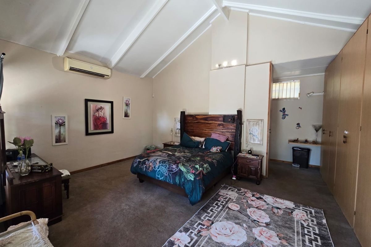 Spacious bedroom featuring high vaulted ceilings, built-in wooden cabinetry, and a wall-mounted air conditioning unit.
