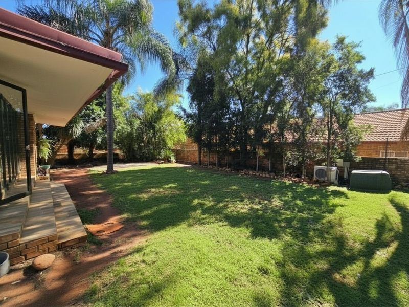 A spacious rear garden featuring a manicured lawn, mature trees, and a covered patio area, providing a private outdoor space for relaxation.